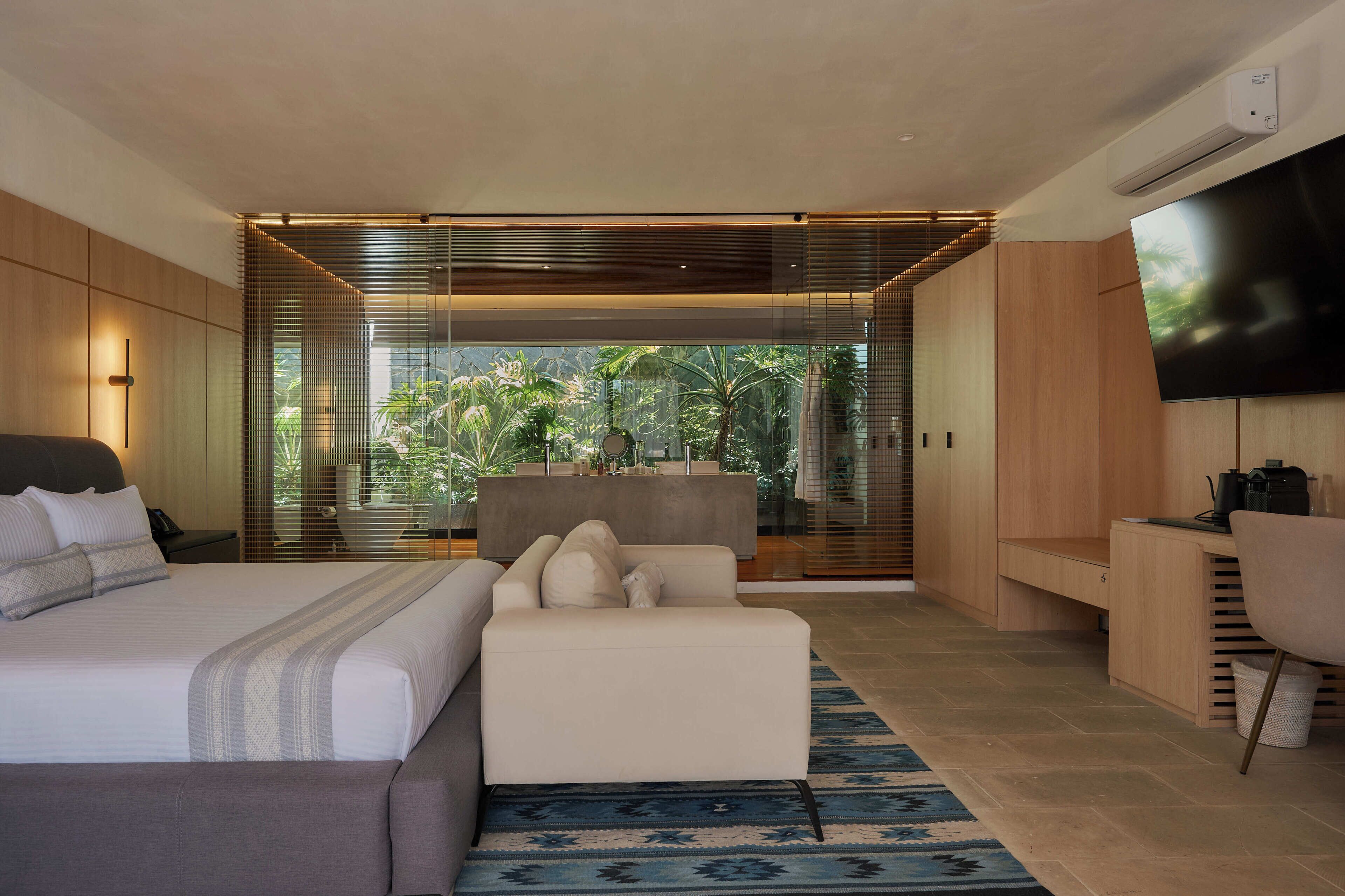 A modern hotel room with a large bed, a sofa, a desk, and a TV.