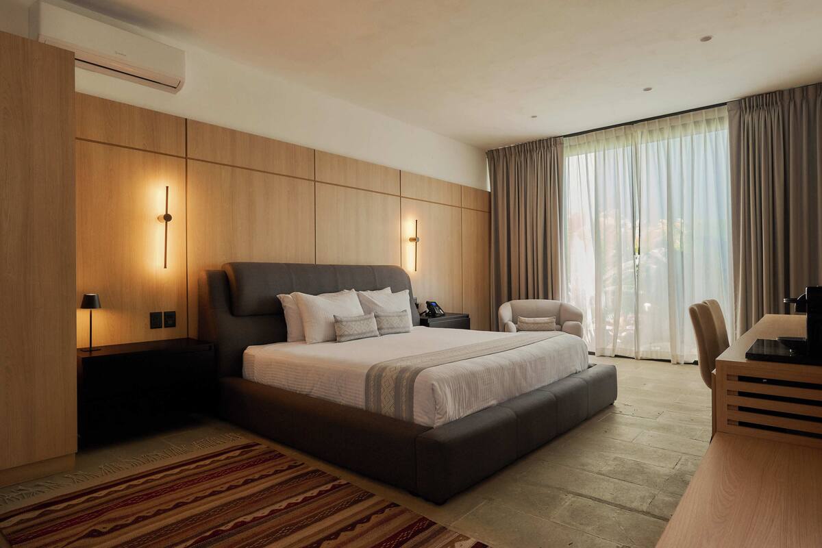 A modern hotel room with a large bed, bedside tables, a desk, and a view of the outdoors.