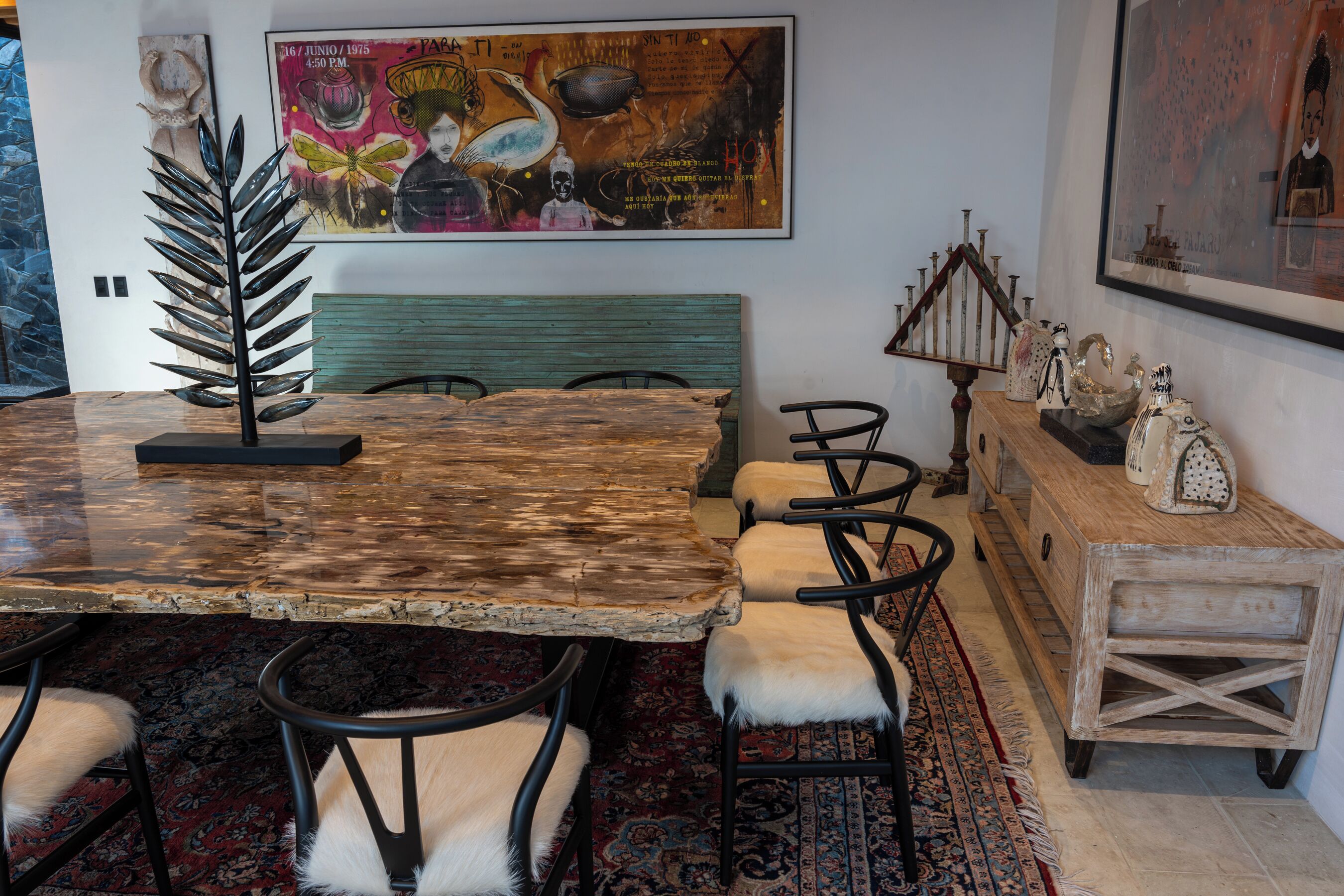 Uma área de refeições com uma mesa de madeira rústica, cadeiras pretas com detalhes de pele branca, um banco estofado verde e um tapete estampado.