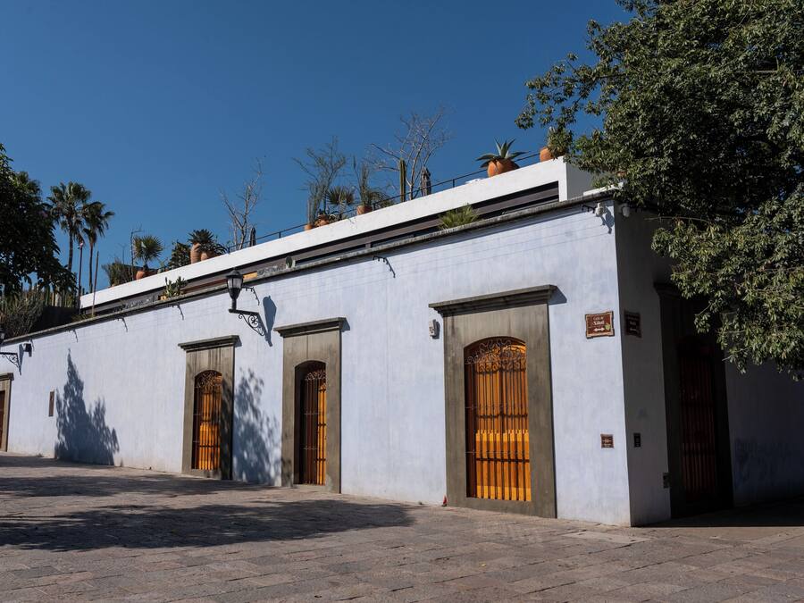 A white building with three arched doors and a balcony with potted plants.