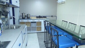 Una cocina con un lavamanos de acero inoxidable, un microondas y una estufa. Hay taburetes altos azules y una mesa con cubierta de vidrio.