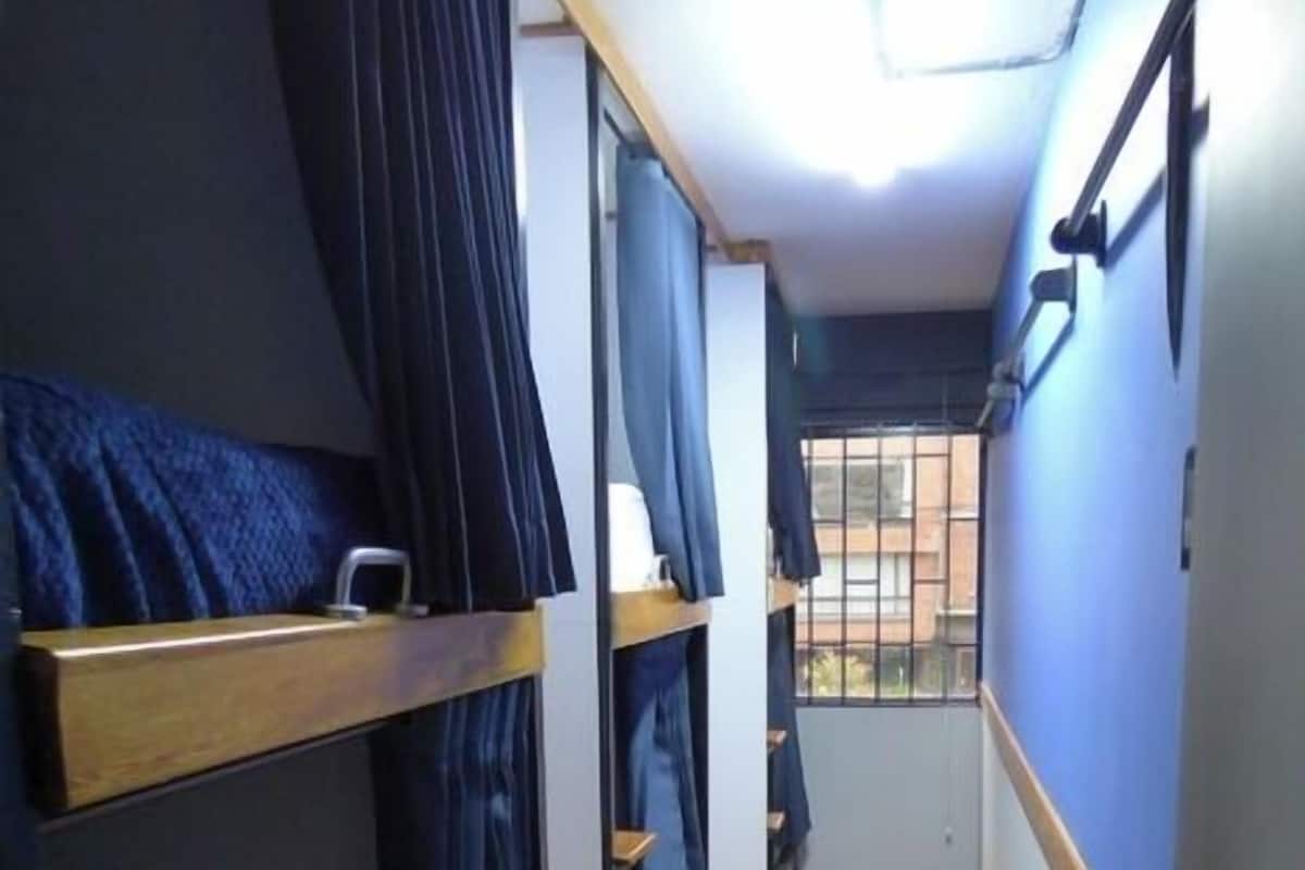 A narrow corridor with bunk beds, wooden flooring, and a window at the end.