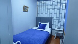 Un dormitorio pequeño y ordenado con una cama individual, una mesita de noche y una ventana con vistas.