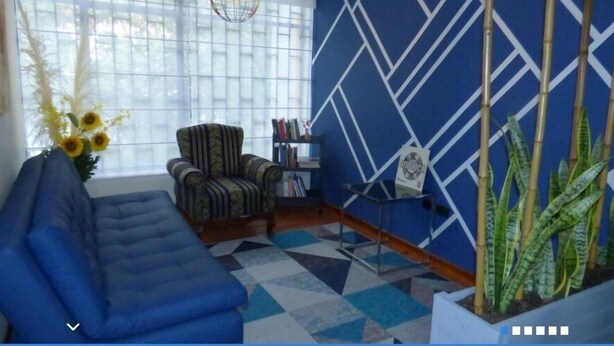 Una sala de estar con un sofá azul, un sillón estampado y una estantería.