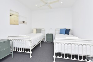 Una camera da letto con due letti singoli, una ventola a soffitto e un comodino.