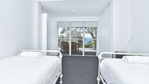 Et hotelværelse med to senge, et lille bord og udsigt gennem en glasdør til en udendørs terrasse.