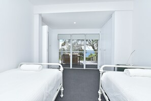 A hotel room with two single beds, a small table, and a view through a glass door to an outdoor deck. - Salt and Serenity (Nelson Bay)