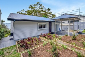 A residential property with a covered outdoor area, a garden with various plants, and a view of the sea. - Salt and Serenity (Nelson Bay)