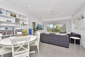 A modern living room with a grey sofa, white dining table, and a TV on a stand. - Salt and Serenity (Nelson Bay)