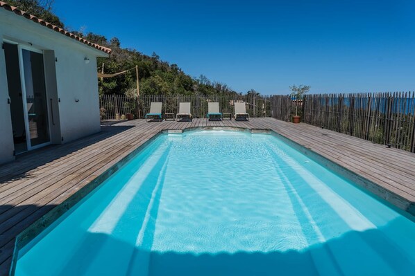 Una piscina rectangular con cubierta de madera, rodeada por una valla y un edificio con una puerta.