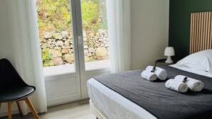 Een slaapkamer met een bed, een stoel, een nachtkastje en uitzicht op groen buiten.