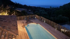 Een houten terras met een zwembad, met uitzicht op een waterpartij en heuvels.