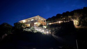 Een huis met twee verdiepingen, met een balkon, omringd door bomen en een klein waterpartij.