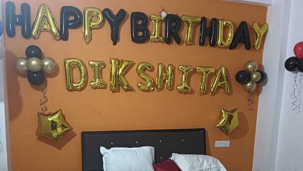 A bedroom with a bed, white bedding, and a birthday decoration on the wall.