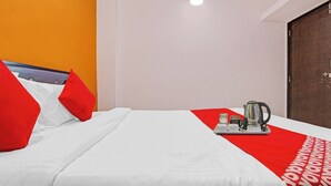A hotel room with a bed, red pillows, a red and white blanket, a coffee maker, and a door.