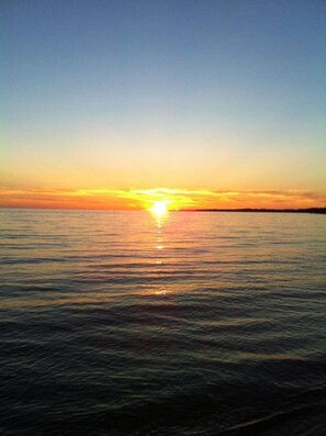 A sunset over a calm body of water. - Cozy Beachside Getaway – Steps from Balm Beach! (Tiny)