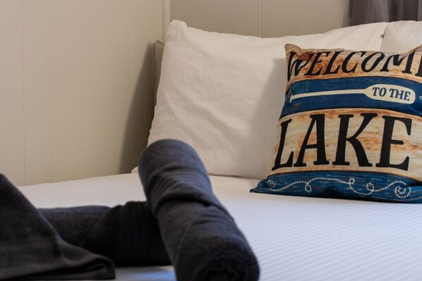 Un lit avec un oreiller sur lequel est brodé le message : « BIENVENUE AU BORD DU LAC ».