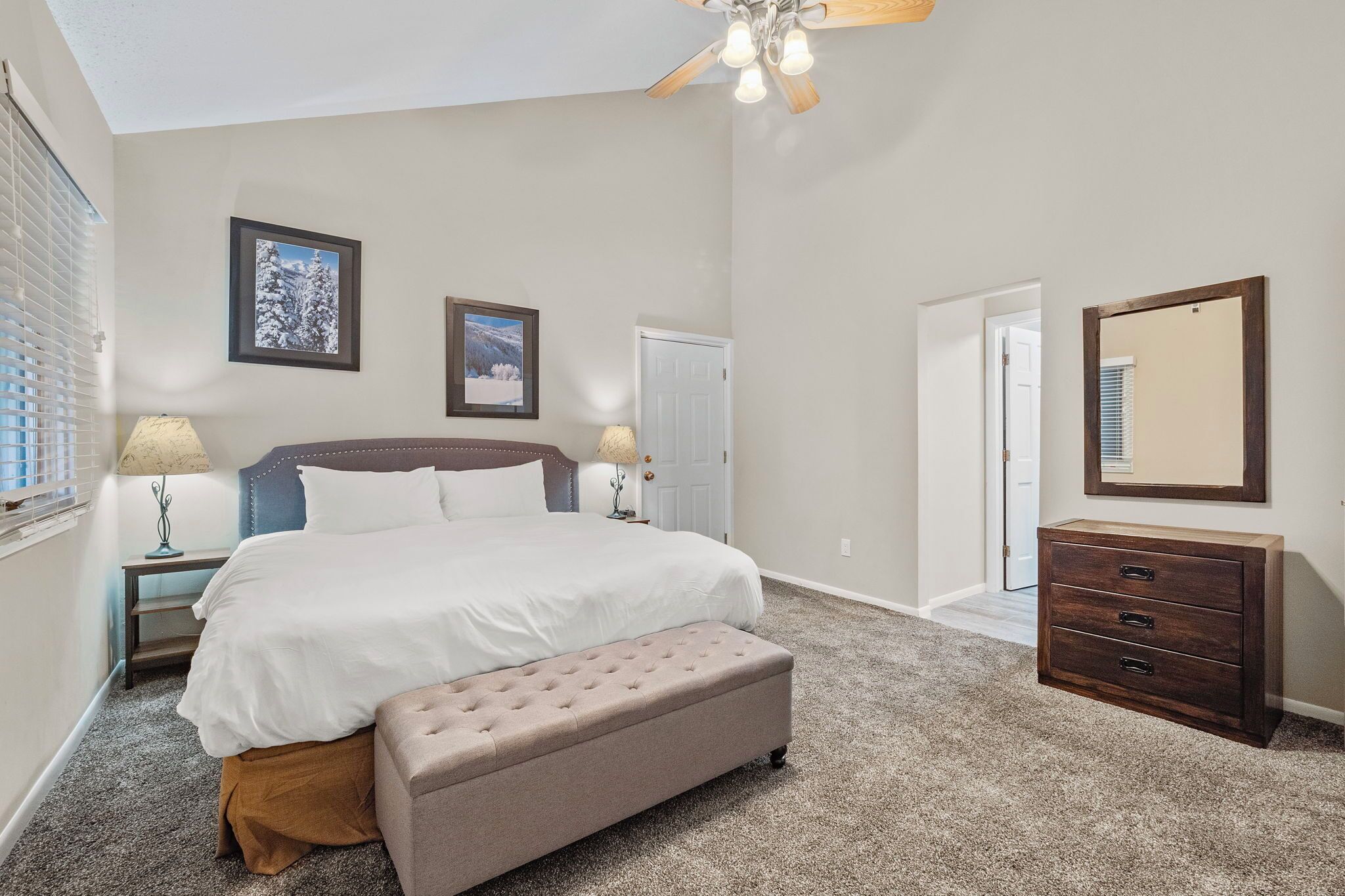 A bedroom with a bed, bench, dresser, and ceiling fan.