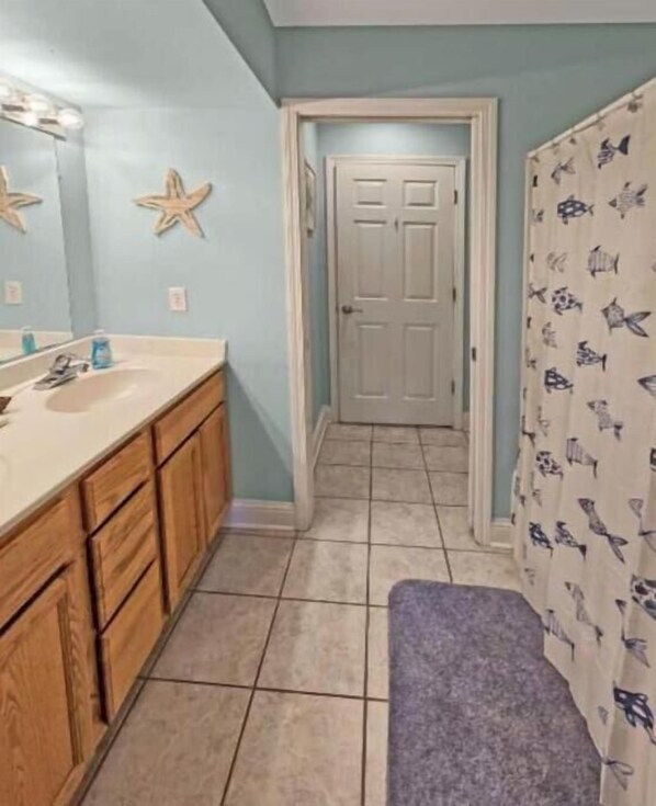 A bathroom with a wooden vanity, a sink, and a shower curtain with fish patterns. - Best location in Biloxi! Walk to the beach! (Biloxi)