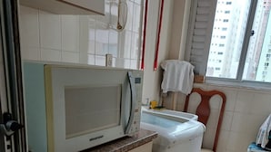 Una cucina compatta con un forno a microonde, una lavatrice e una sedia.