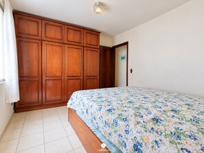 A bedroom with a bed, wooden wardrobe, and a door. - Ap Vista Mar - Ed Belo Mar - BC (Balneário Camboriú)