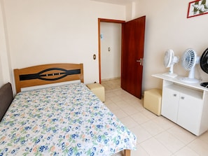 A bedroom with a bed, a wooden door, a white cabinet, and two standing fans. - Ap Vista Mar - Ed Belo Mar - BC (Balneário Camboriú)