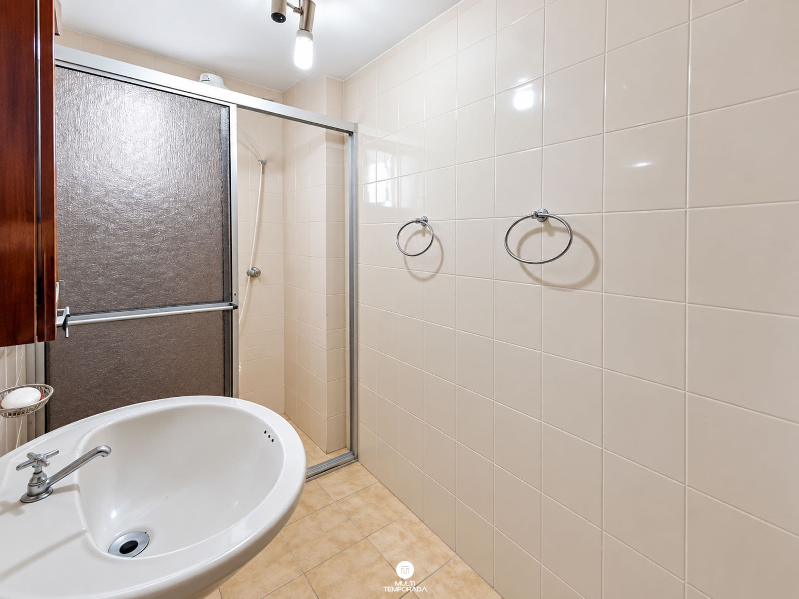 Ein Badezimmer mit einem weißen Waschbecken, einer Duschkabine aus Glas und einem Handtuchhalter an der Wand.