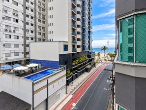 A multi-story hotel with a rooftop pool, a street with a red bike lane, and a view of the beach. - Ap Vista Mar - Ed Belo Mar - BC (Balneário Camboriú)