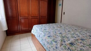 Una camera da letto con un ampio armadio in legno, una coperta con motivi floreali e un pavimento piastrellato.