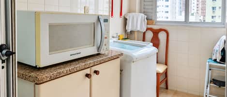 Cocina compacta equipada con microondas, lavadora y ventana con vista a edificios.