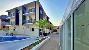 A modern residential building with a swimming pool, lounge chairs, and a paved walkway. - 989 Apartments (Abuja)