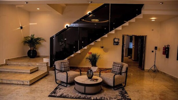 A modern living room with a staircase, a round coffee table, and two armchairs. - 989 Apartments (Abuja)