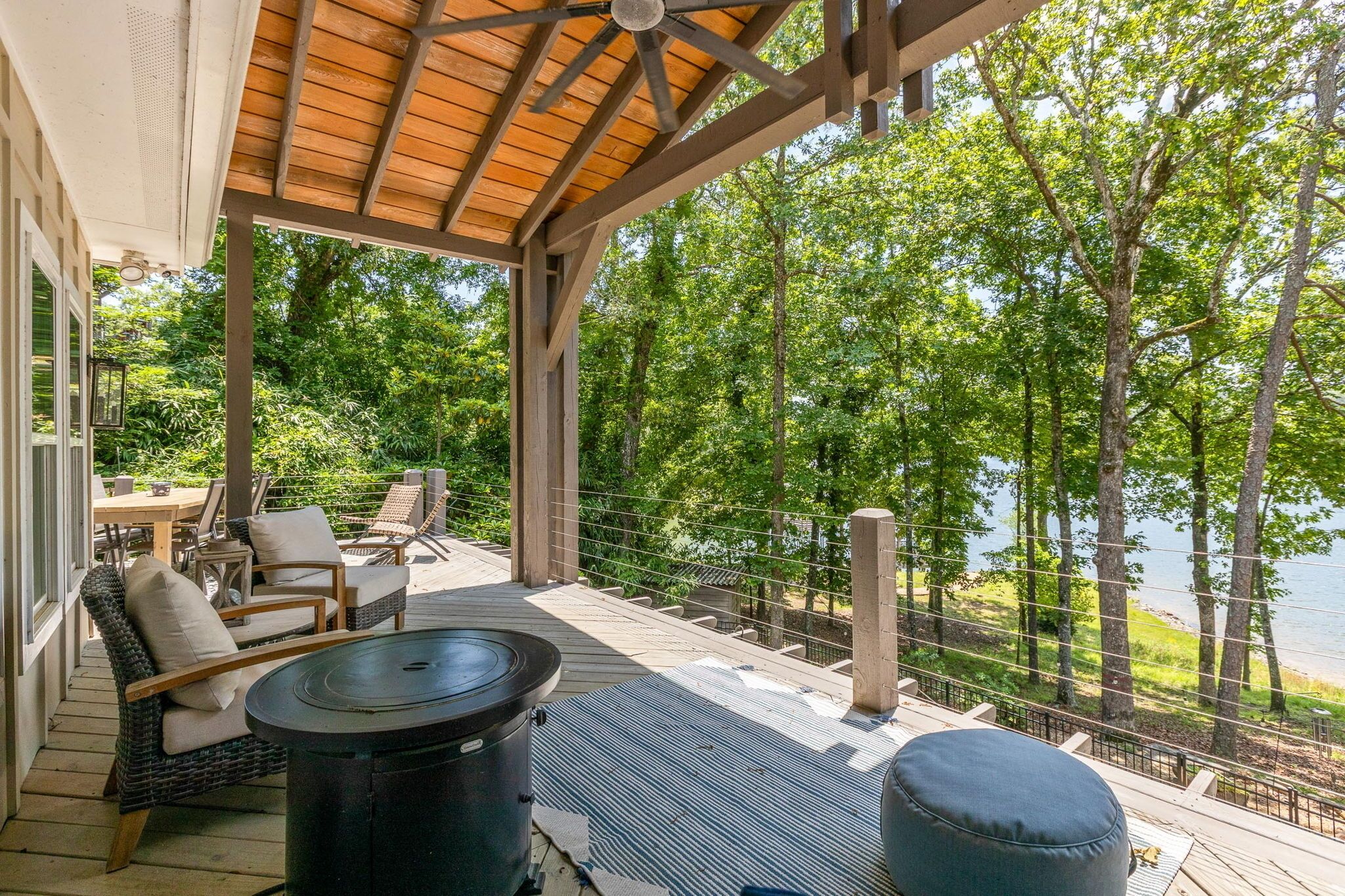A covered outdoor deck with wicker furniture, a round table, and a view of a lake.