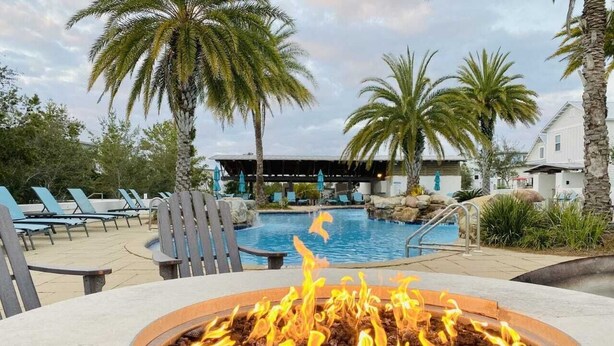 Un área de piscina con sillones de descanso, una chimenea y palmeras.