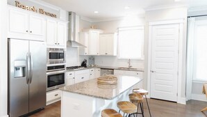 Una cocina moderna con armarios blancos, electrodomésticos de acero inoxidable y una isla central con taburetes.