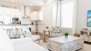 Una sala moderna con un amplio sofá modular, una mesa de centro y un comedor con muebles blancos de cocina al fondo.