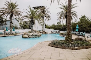 Une piscine bordée de palmiers, avec des chaises longues et un bâtiment en arrière-plan.