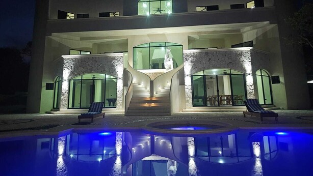 Una casa moderna de dos pisos con piscina, amplios ventanales y una escalera que lleva al nivel superior.