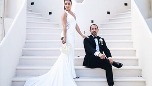 Una pareja en una escalera con un edificio blanco y una escultura al fondo.
