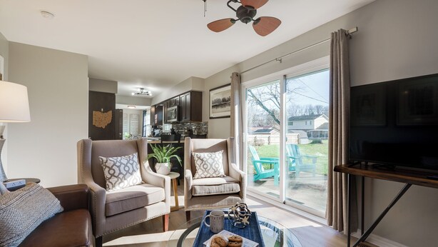 Ein modernes Wohnzimmer mit einer Couch, Sesseln, einem Couchtisch mit Keksen, einem Fernseher und einem Deckenventilator.