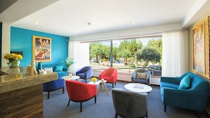 A hotel lobby with a blue wall, a wooden reception desk, and several colorful chairs and sofas arranged around a central coffee table. - MURU HOMELY HOTEL (Cusco)