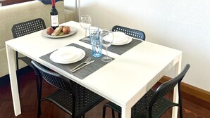 Un coin repas avec une table blanche dressée pour quatre personnes, des chaises noires, un miroir en osier et une œuvre d’art murale.