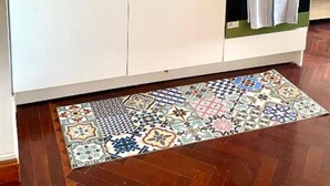 Une cuisine compacte équipée d’un évier, d’une cuisinière et d’un four, avec un crédence bleue et un tapis à motifs.