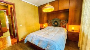 Ein Schlafzimmer mit einem Bett, einem hölzernen Kopfende, Nachttischlampen und einem Spiegel.