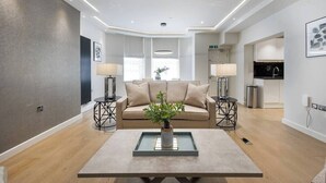 Una sala de estar moderna con un sofá, una mesa de centro y lámparas. Se ve un área de cocina al fondo.