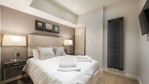 Una habitación de hotel moderna con una cama grande, dos mesitas de noche con lámparas, un radiador y un televisor de pantalla plana montado en la pared.