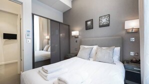 A hotel room with a bed, bedside tables, a mirror, and a TV mounted on the wall.