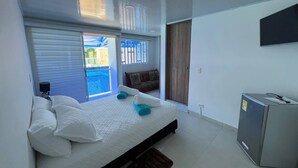 Une chambre moderne avec un grand lit, un téléviseur fixé au mur et une porte coulissante donnant sur un balcon.