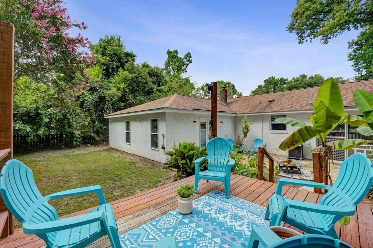 Une terrasse avec des chaises turquoise, une nappe à motifs et une maison en arrière-plan.