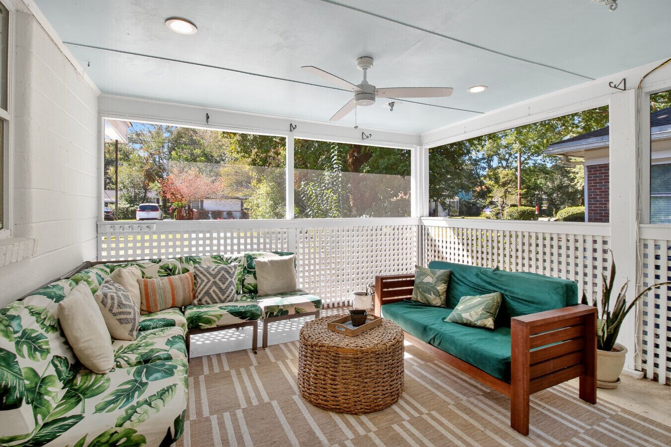 A covered porch with two sofas, a woven coffee table, and a ceiling fan.